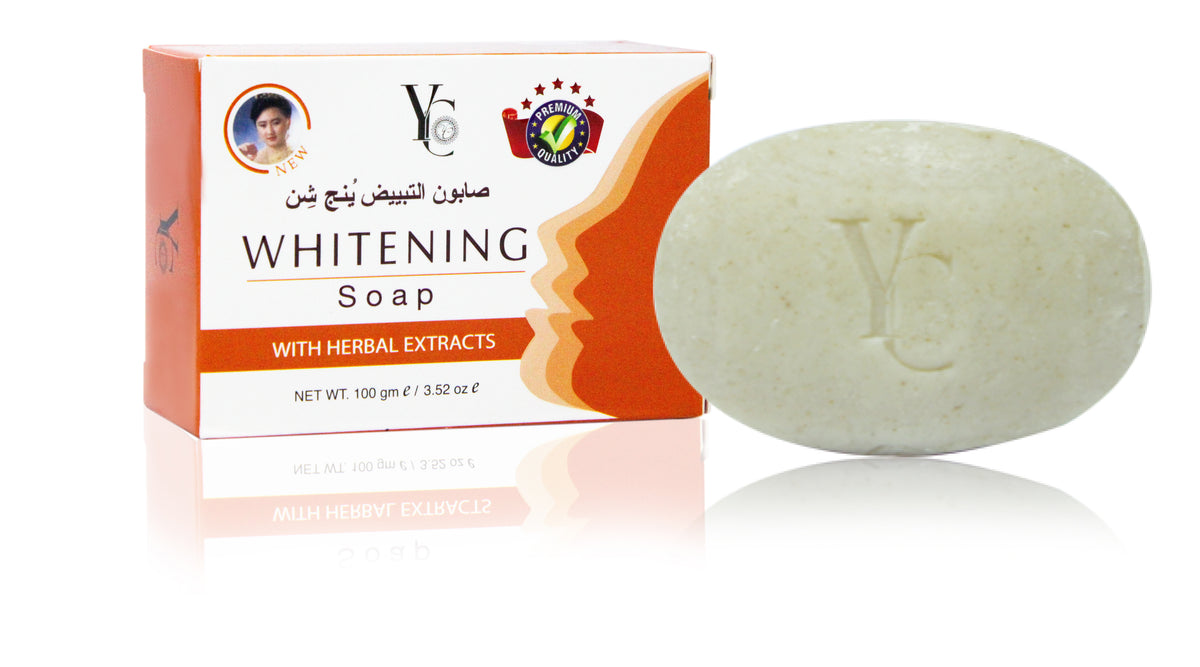 A bar of whitening soap next to its retail box. The soap is a pale, textured off-white oval with an embossed 'YC' logo.