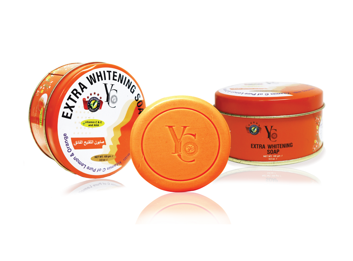 Three containers of YC Extra Whitening Soap arranged on a white reflective background: one upright can with a white label, one orange tin showing the front label, and one orange lid placed in front.